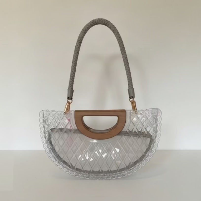 A clear PVC semi-circular handbag with a textured diamond pattern, a brown faux-leather top handle, and a gray braided shoulder strap, shown on a plain white background.