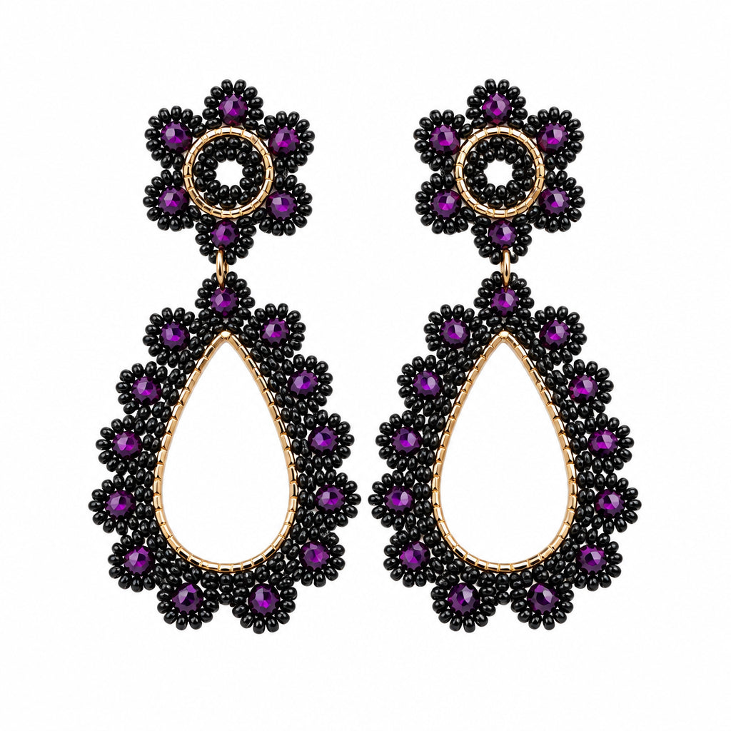 A pair of gold-tone dangle earrings with dark purple beaded floral tops and teardrop-shaped lower drops, displayed on a white jewelry stand.