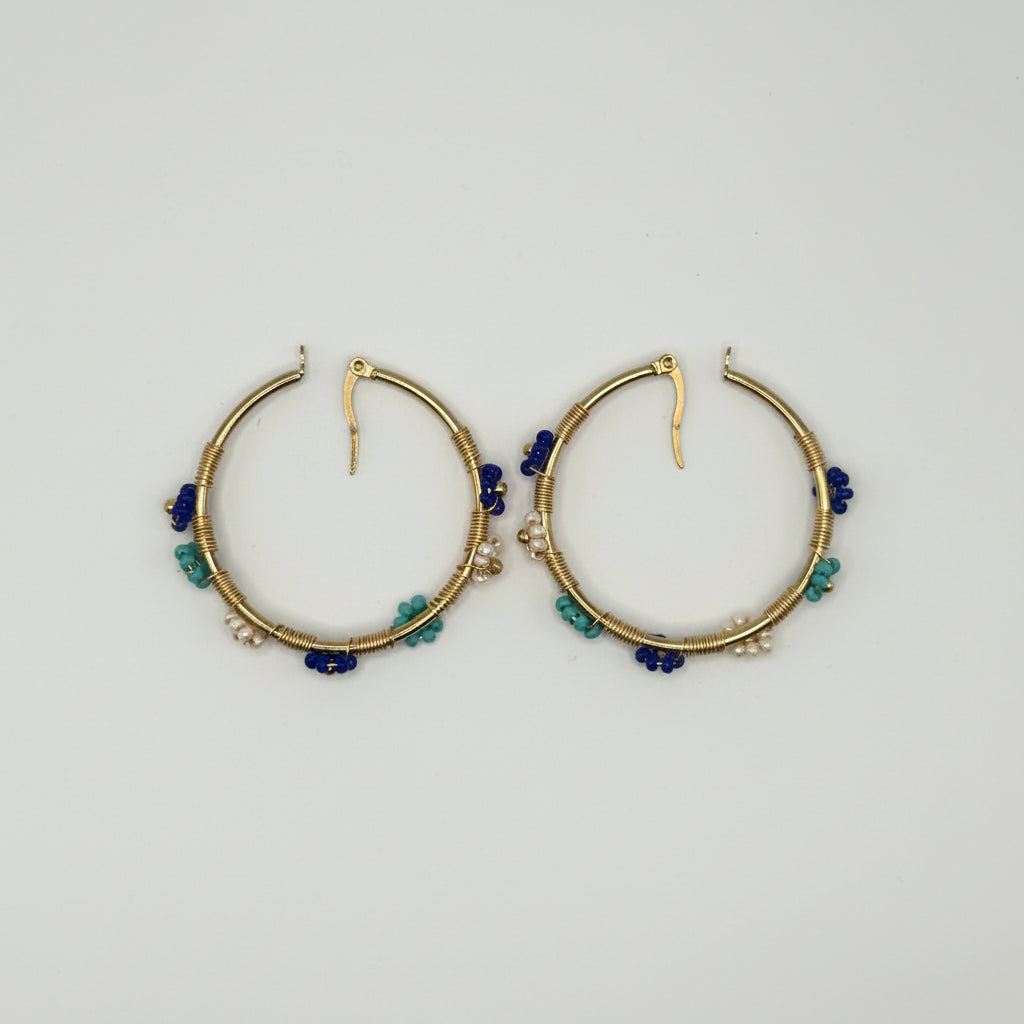 A pair of gold hoop earrings decorated with small blue and green beads, displayed on a plain white background.