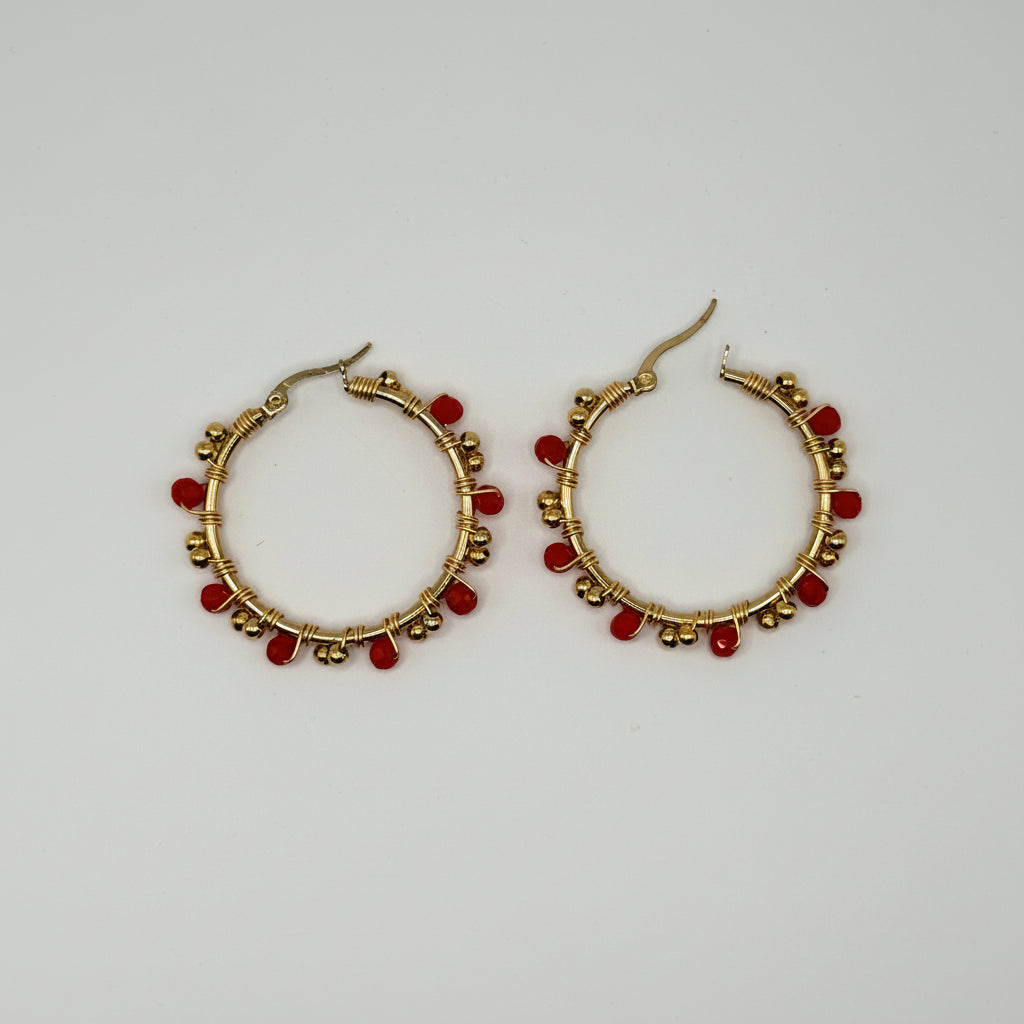 A pair of gold hoop earrings decorated with small red beads, displayed on a plain light gray background.