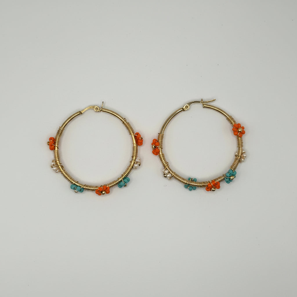 A pair of gold hoop earrings decorated with small orange and teal beads, displayed on a plain light gray background.