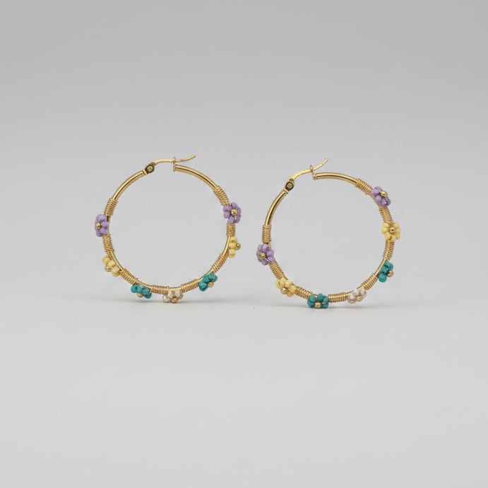A pair of gold hoop earrings decorated with small multicolored beads, displayed on a plain white surface.