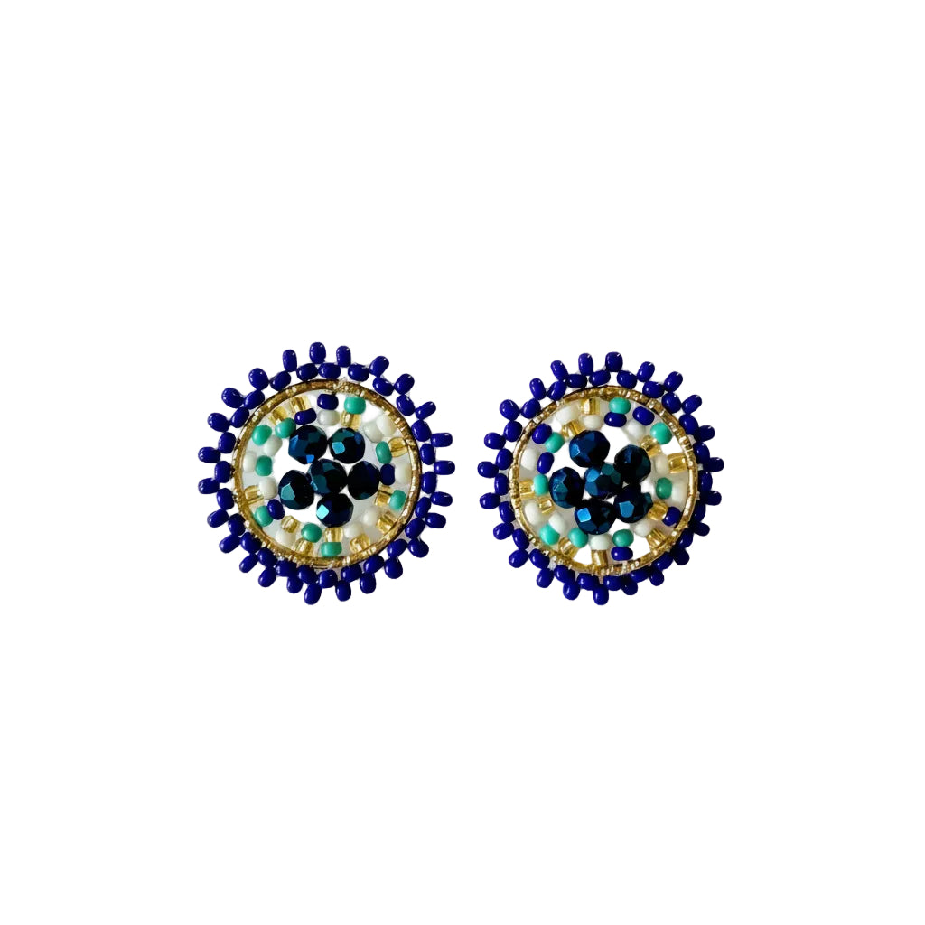 A pair of handmade circular beaded earrings with a blue outer border, gold-toned inner ring, and a central white, black, and turquoise pattern, displayed on a light off-white background.