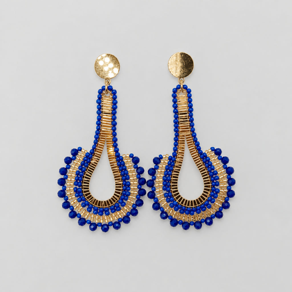A pair of handmade teardrop dangle earrings with gold-plated studs and blue and gold beaded details, displayed on a white card.