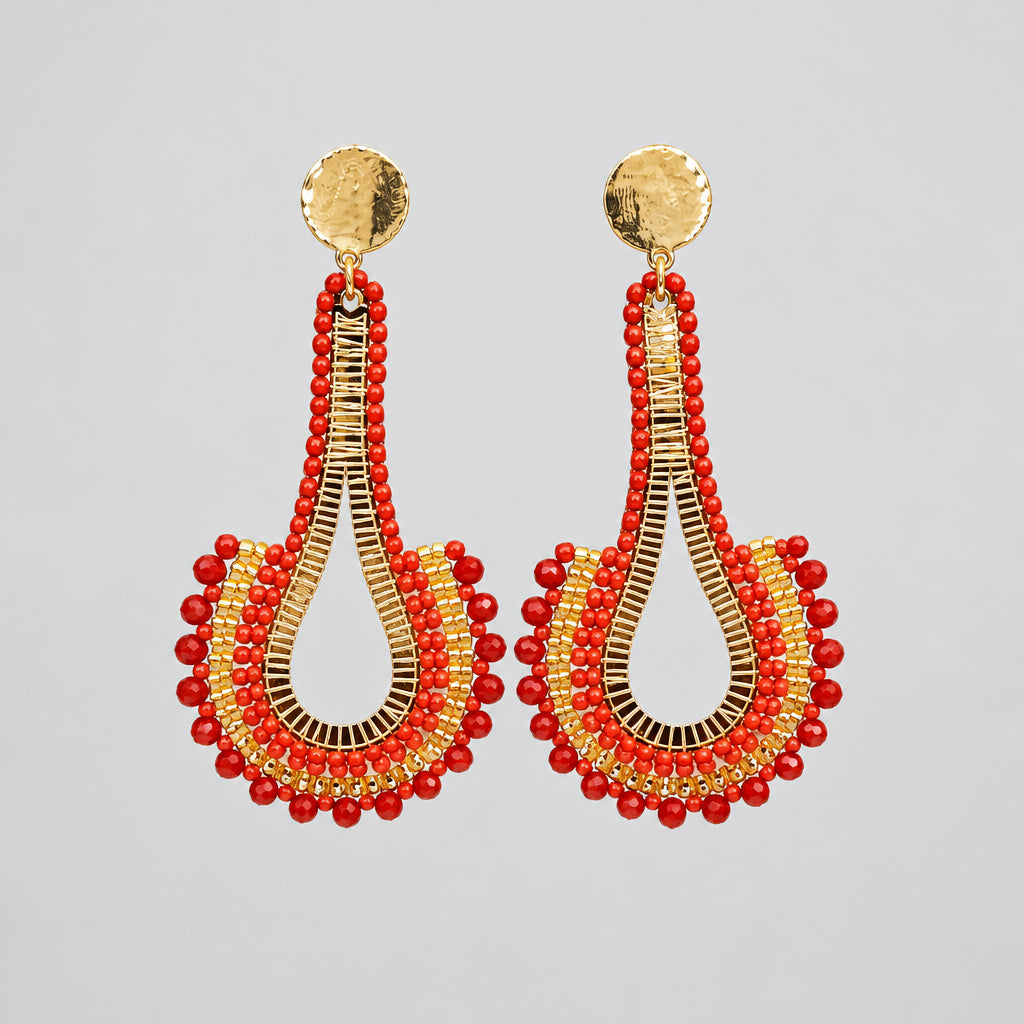 A pair of handmade dangle earrings with red beaded fringe and gold-toned metal details, displayed on a clear plastic card against a white background.