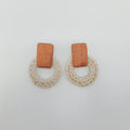 Pair of earrings with wooden top and beige circular bottom on a light gray background
