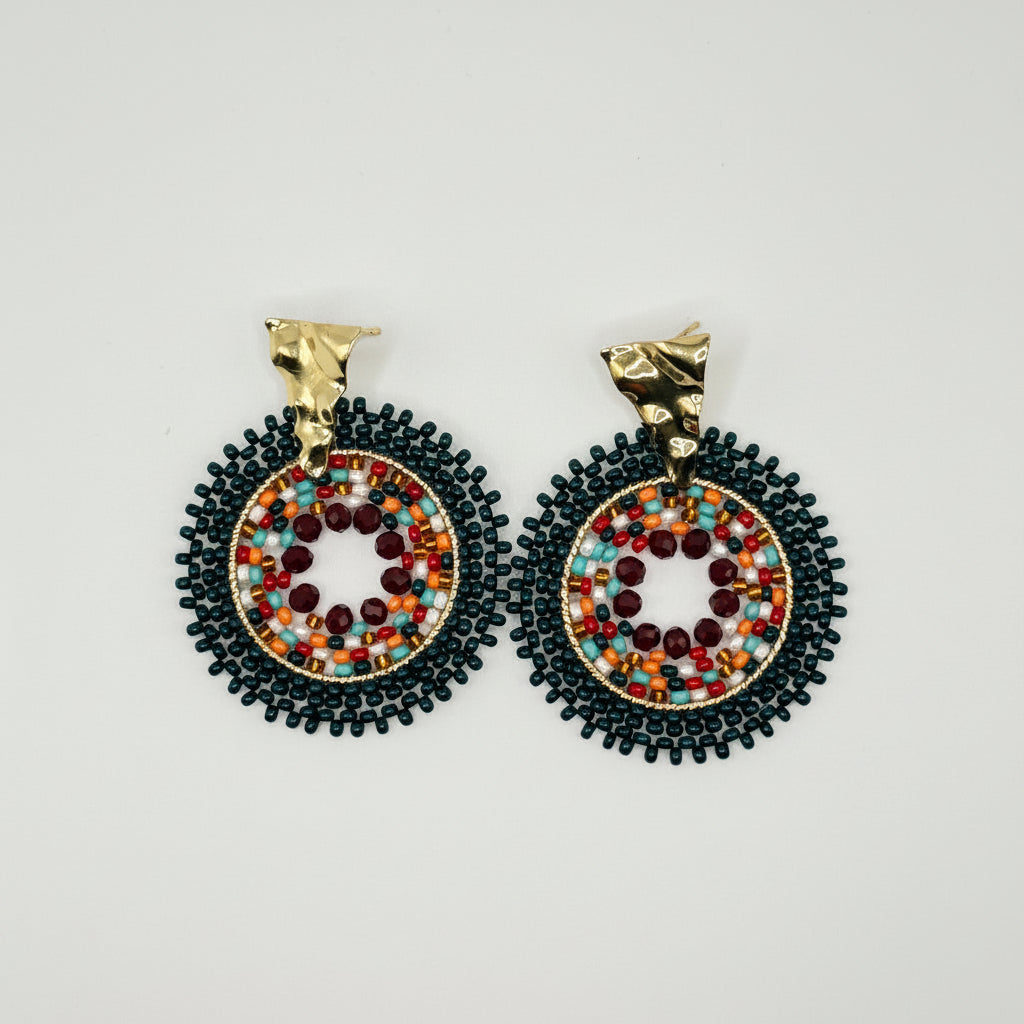 A pair of handmade beaded earrings with gold-tone posts and circular drop charms featuring black beaded borders and colorful bead centers on a light gray background.