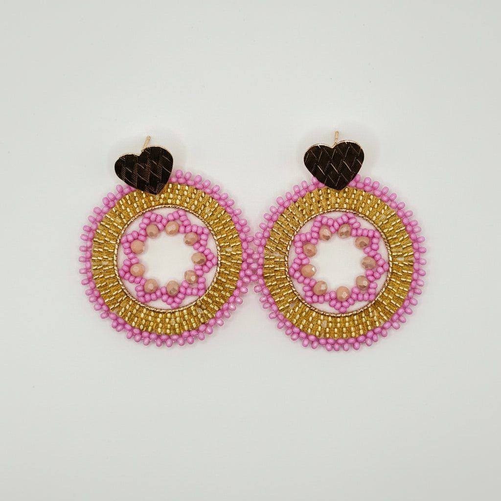 A pair of handmade beaded earrings featuring circular designs with pink and gold seed beads, accented by small dark brown heart-shaped studs on a plain white background.