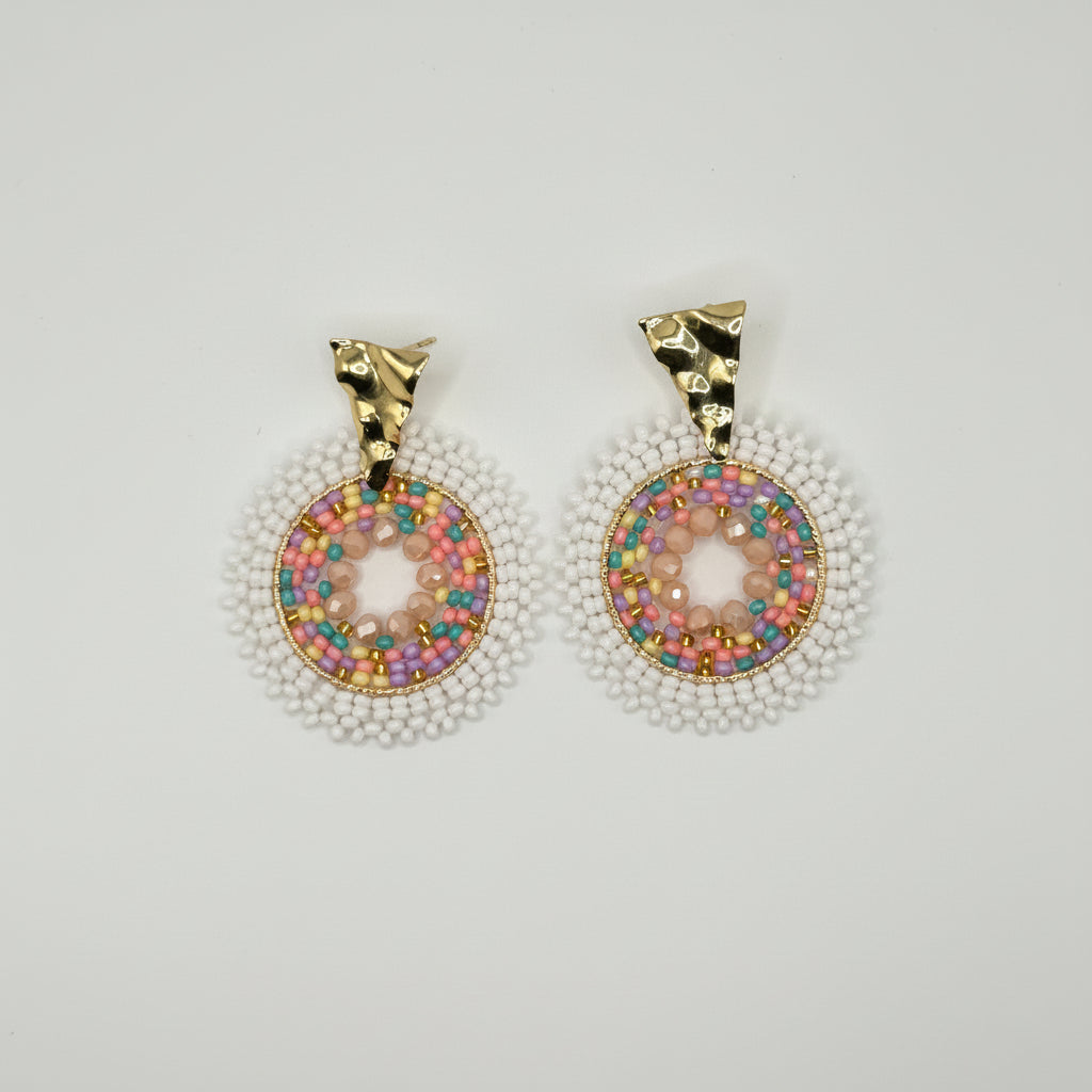 A pair of dangling earrings with gold-toned tops and circular donut-shaped charms covered in iridescent multicolor rhinestones, surrounded by white pearl-like beads, on a plain light gray background.