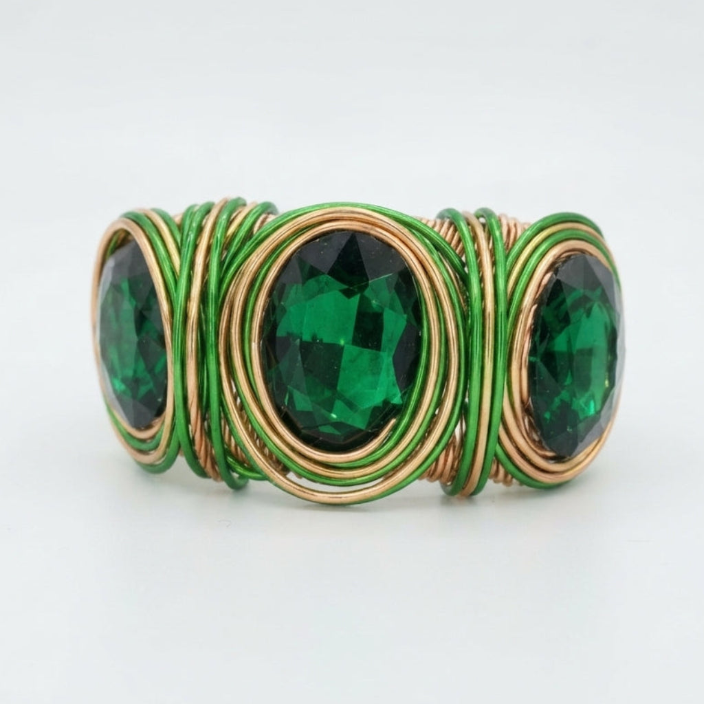 A wrap-style ring featuring three oval-cut emerald green gemstones set in gold-toned metal, surrounded by tightly wrapped green and gold wire on a clean white background.