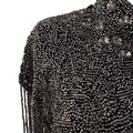 A close-up of a heavily beaded black garment or accessory with a high collar, featuring large faceted clear rhinestones and long dangling fringe, displayed on a mannequin against a plain light background.