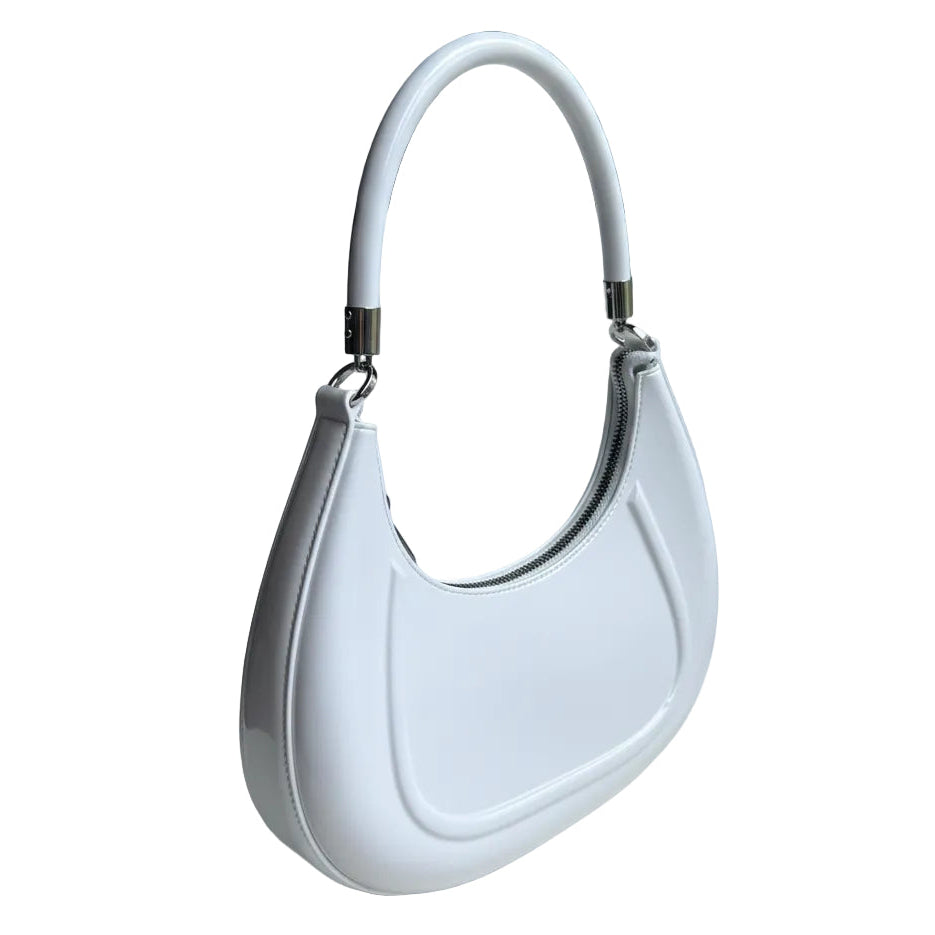 White handbag held by a hand on a white surface with a blurred background
