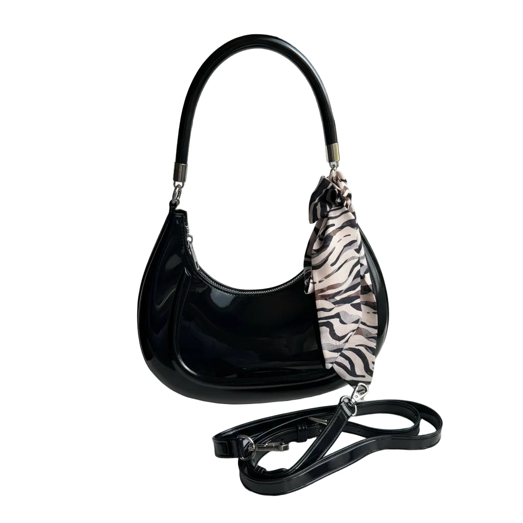 Black handbag with a zebra print strap held by a person, placed on a white surface.