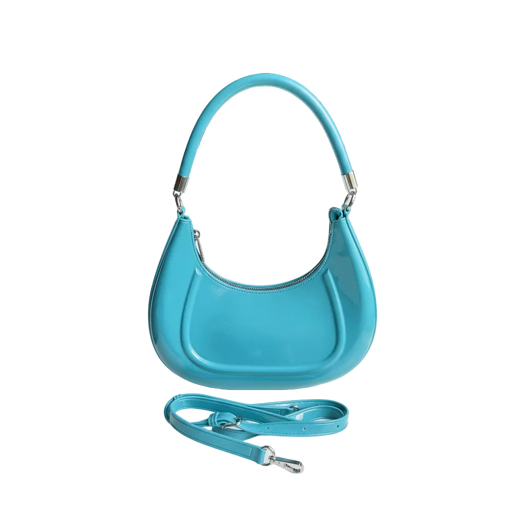Blue handbag with a matching strap held by a hand on a white surface.