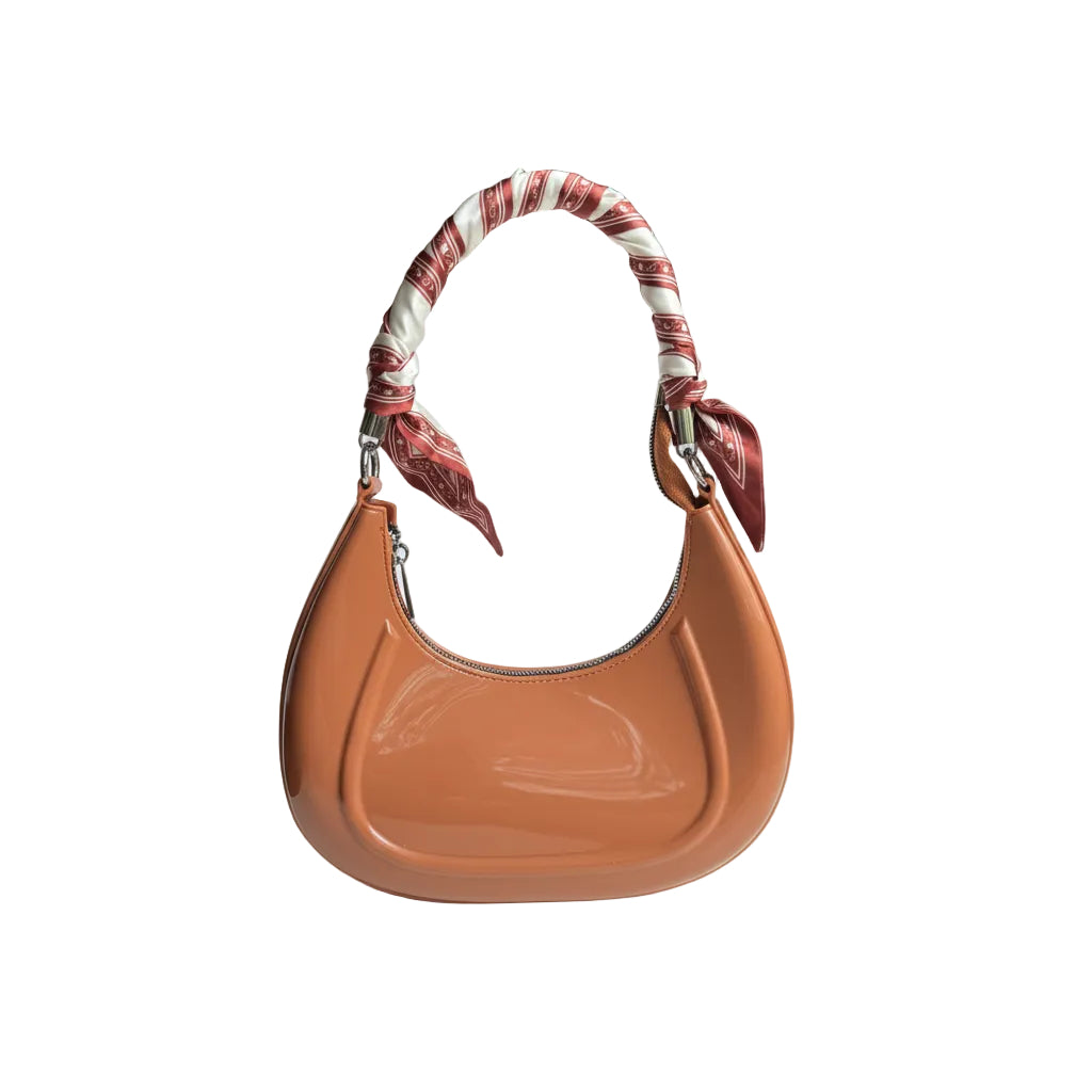 Brown handbag with a patterned strap held by a hand on a white surface.