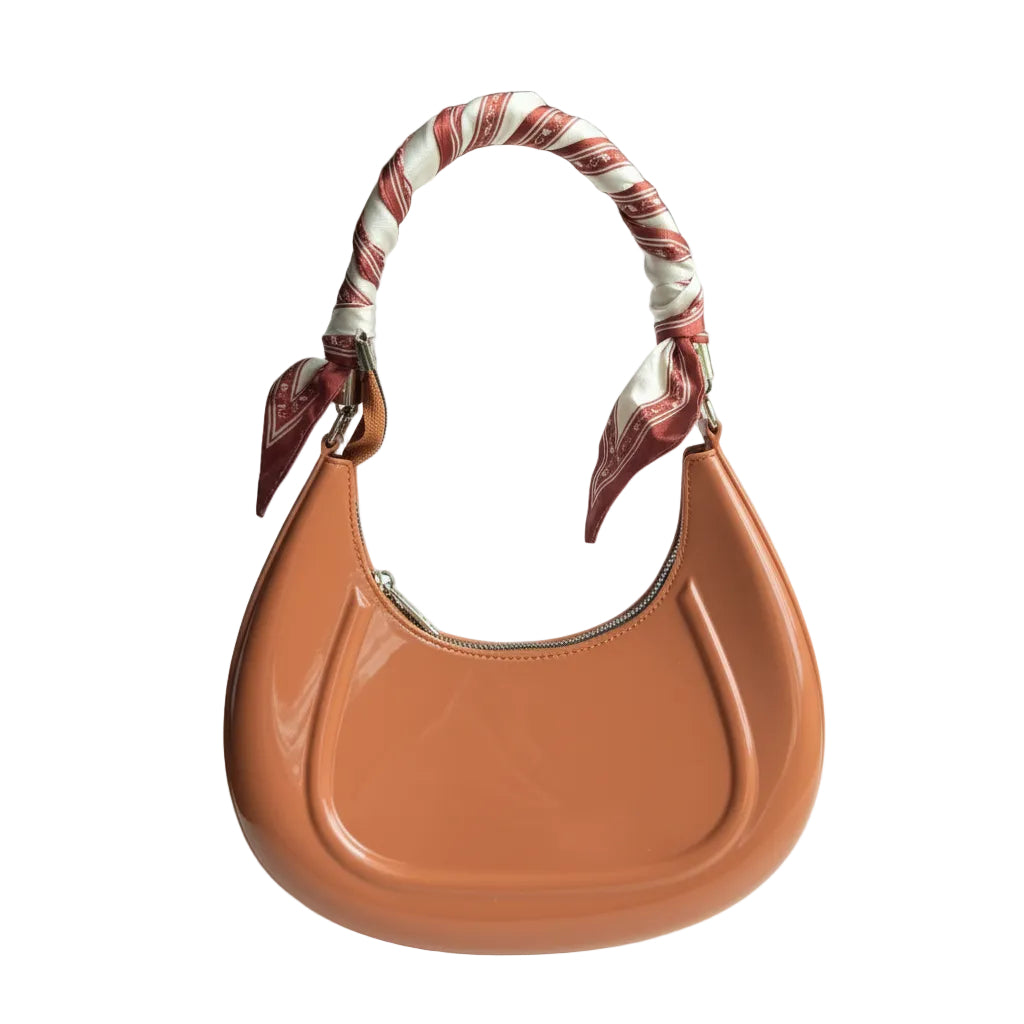 Brown handbag with a patterned strap held by a hand on a white surface.