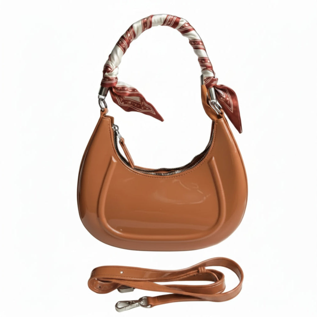 Brown leather handbag with a matching strap held by a person's hand on a white surface.
