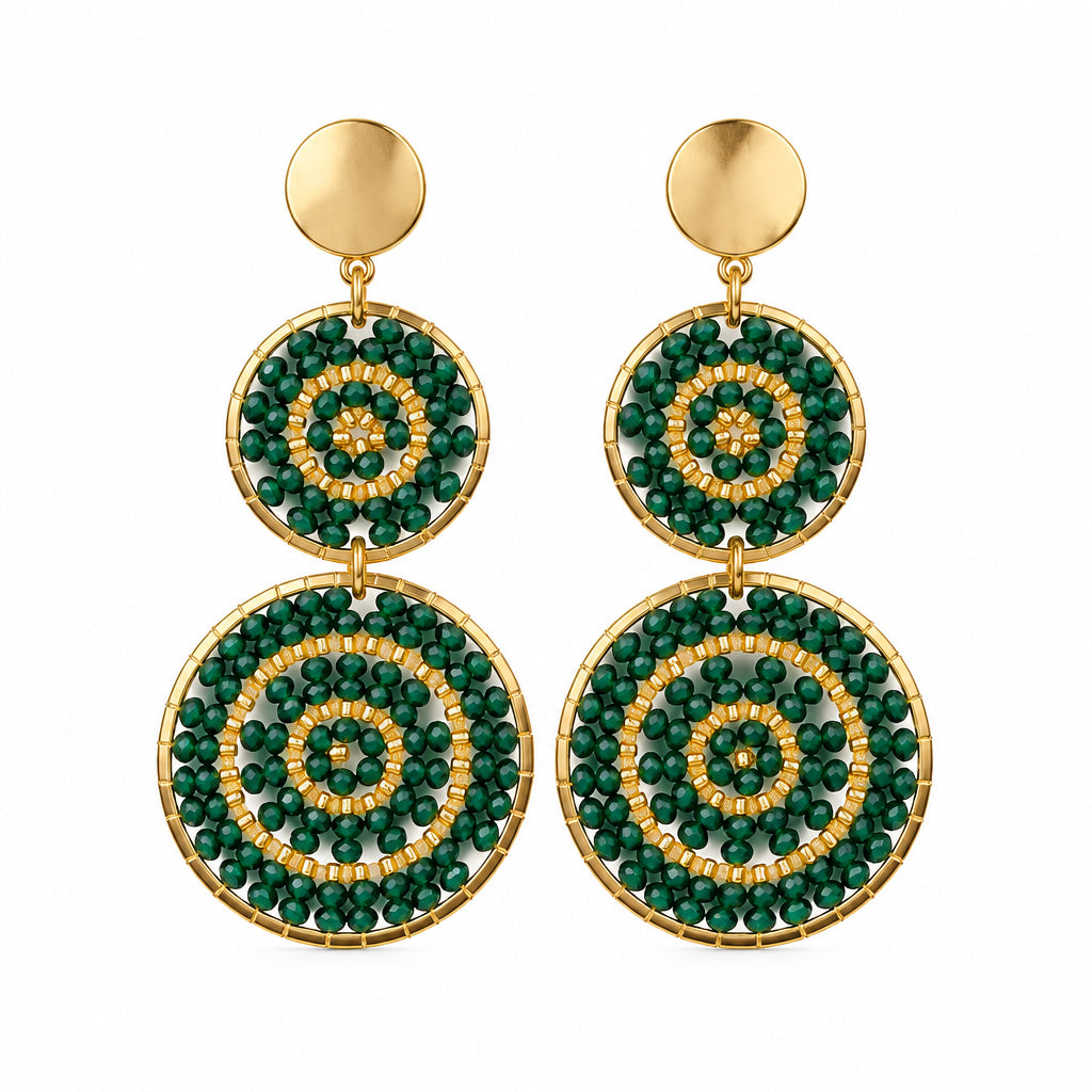 A pair of gold-tone dangle earrings with circular green and white mandala-style patterns, displayed on a white jewelry stand.