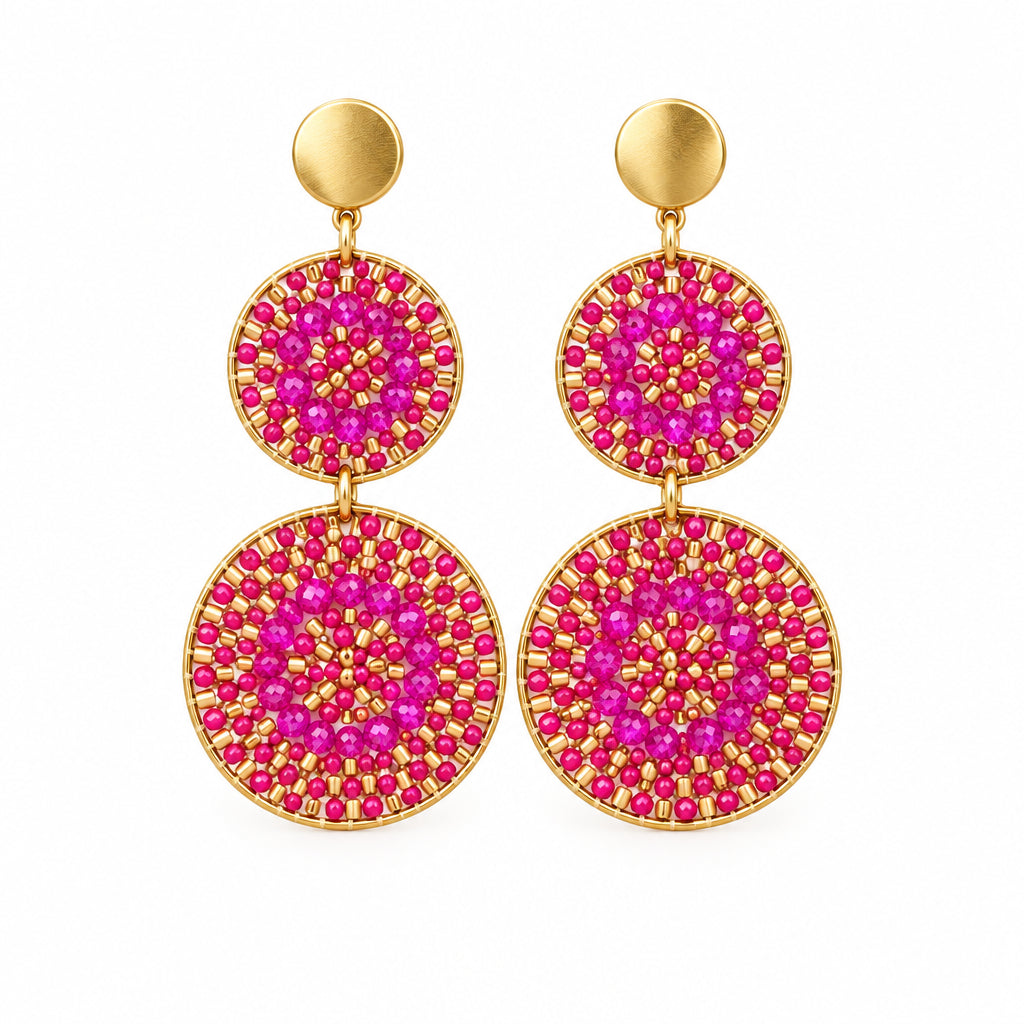 A pair of round drop earrings with pink glittery circular discs and gold-toned studs, displayed on a white backing card labeled stainless steel.