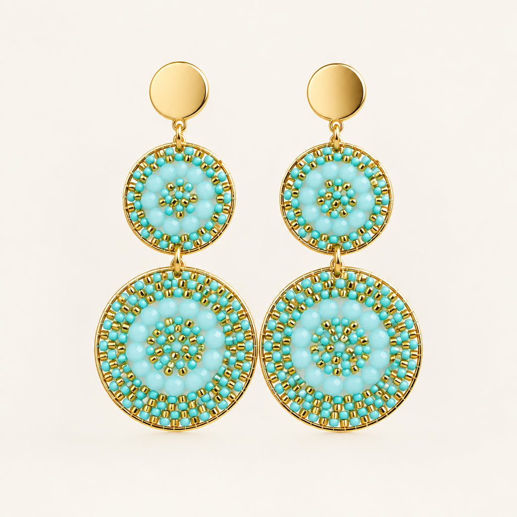 A pair of gold-tone dangle earrings with three stacked circular turquoise and green mandala-patterned discs, displayed on a white mannequin bust.