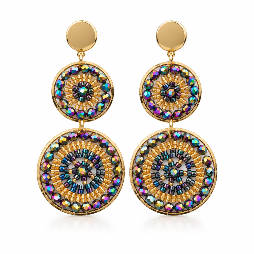 A pair of gold-toned dangle earrings with circular mandala-style charms featuring iridescent multicolor rhinestones, displayed on a white jewelry stand.