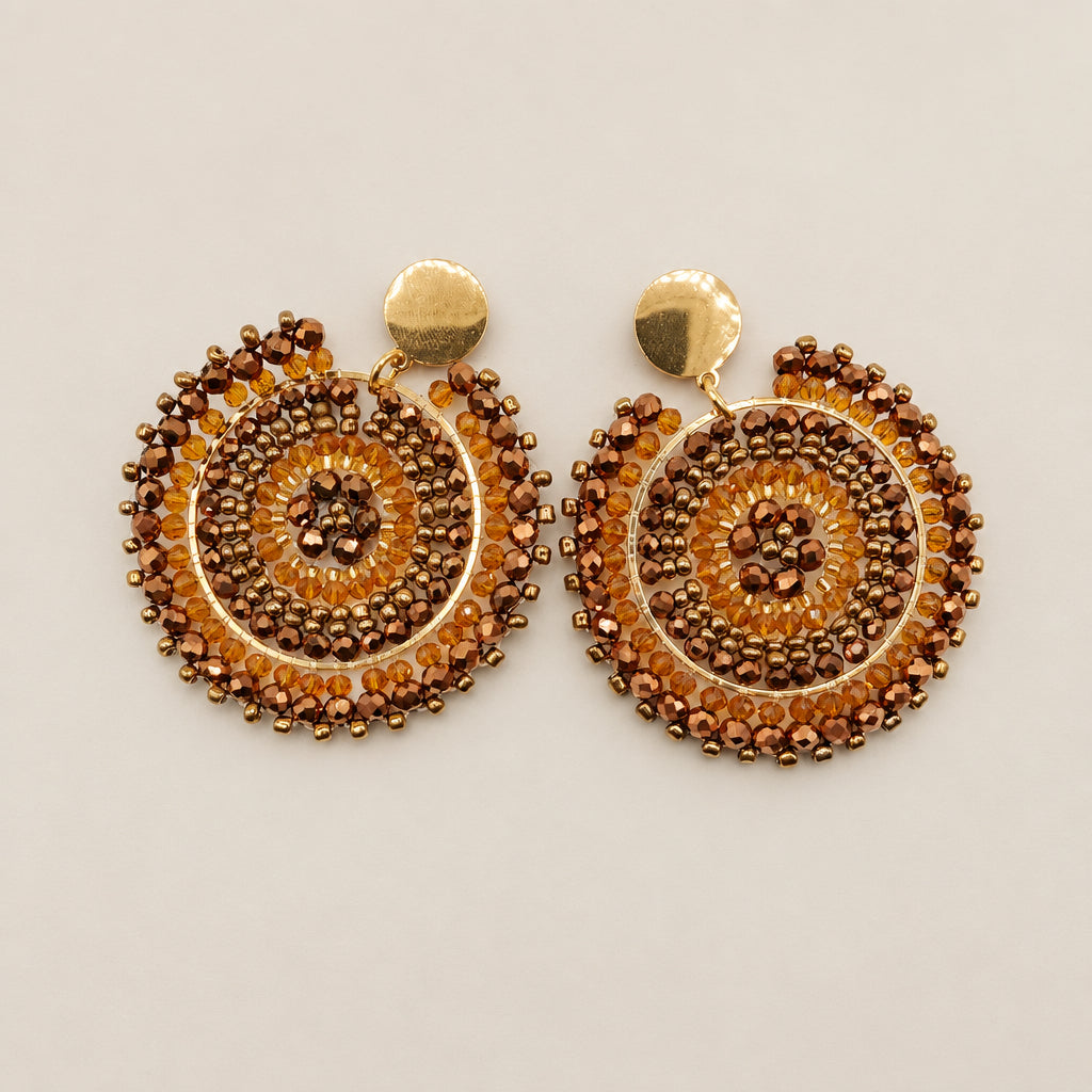 A pair of gold-toned circular dangle earrings with intricate brown beaded concentric patterns, displayed on a white background.