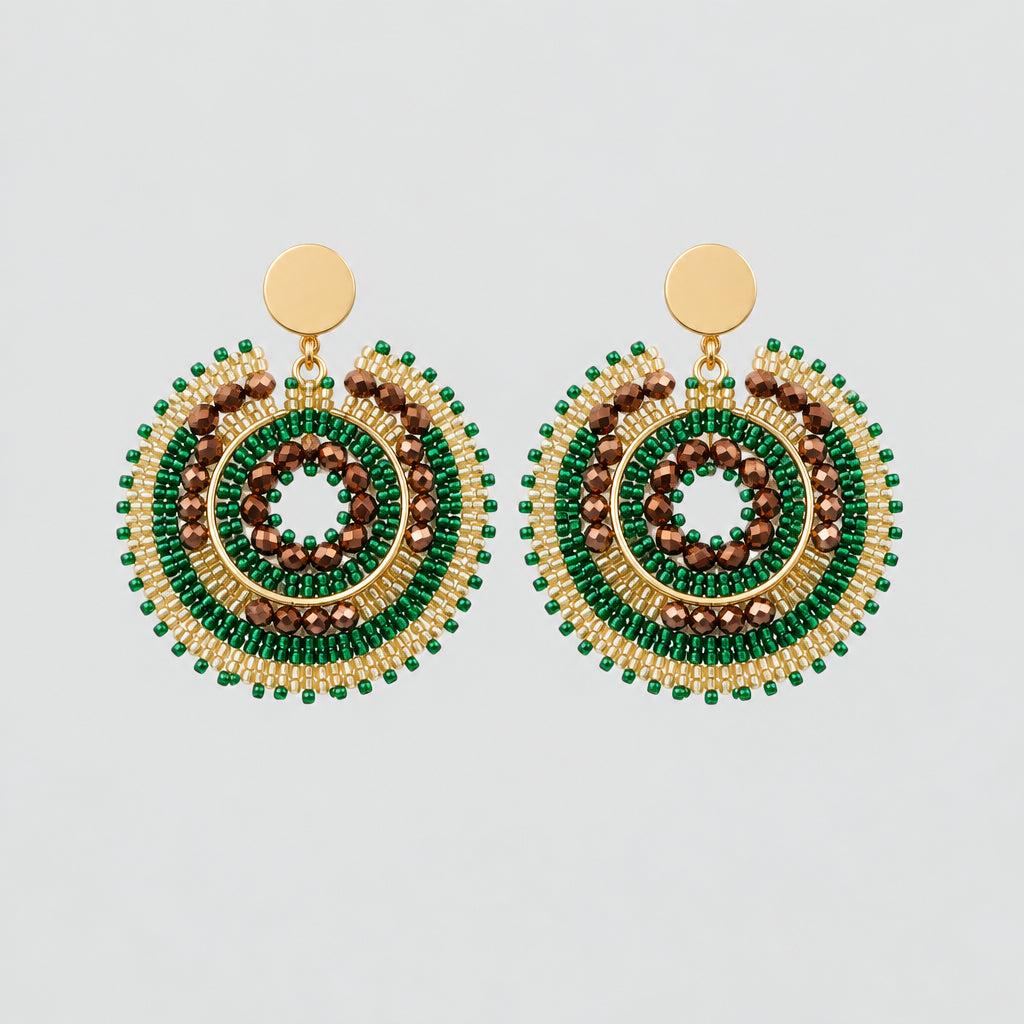 A pair of handmade beaded earrings with green, gold, and white spiral patterns, attached to a small white display card on a white background.