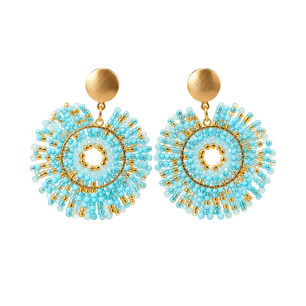 A pair of handmade beaded earrings with light blue and gold circular patterns, displayed on a small white card against a white textured background.