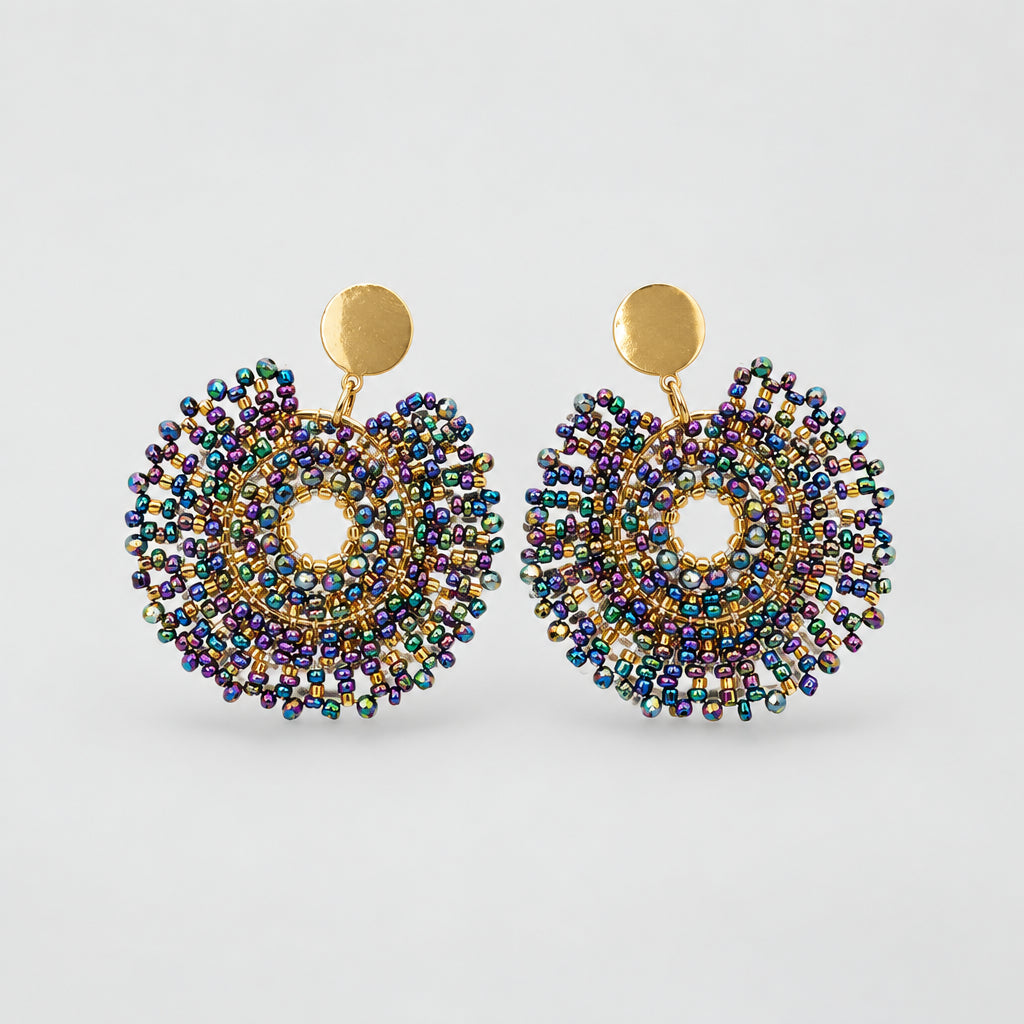 A pair of handmade beaded earrings with gold-tone posts, featuring intricate multicolor seed beads in shades of blue, purple, green, and pink, arranged on a small white card against a white background.