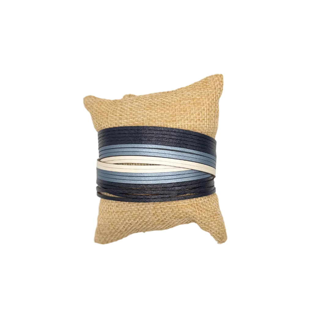 A small square jute pillow with a central wrap of horizontal striped ribbon in navy, blue, gray, and cream, set against a plain white background.