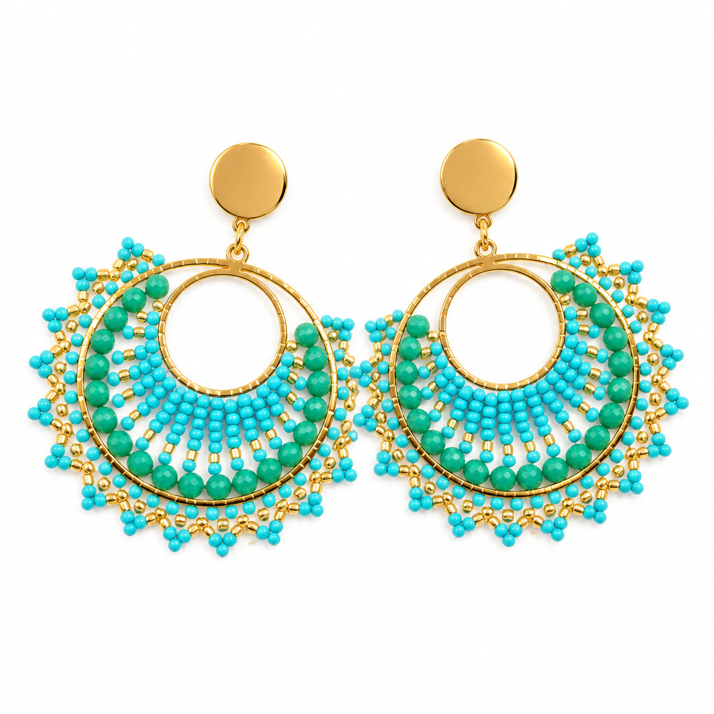 A pair of bohemian-style dangle earrings displayed on a white jewelry stand. The earrings feature turquoise and light blue beaded fringe with gold-tone metal hoops and brown stud backs.