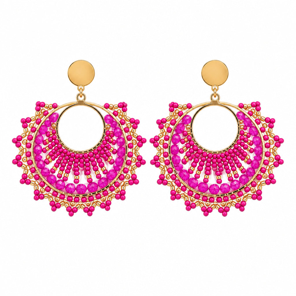 A pair of gold-toned dangle earrings with bright pink beaded circular hoops, displayed on a white backing card against a white background.