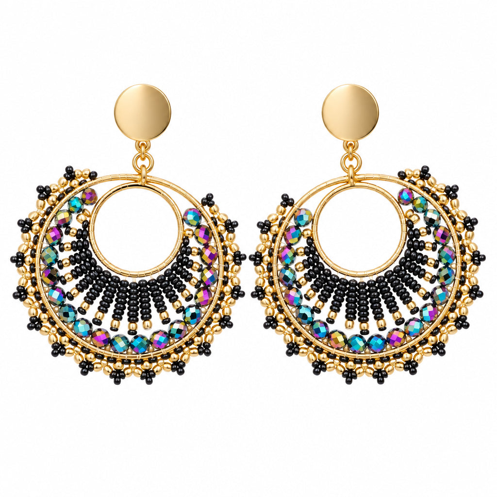 A pair of gold-toned statement earrings with circular cutouts, black beaded detailing, and multicolor rhinestone accents, displayed on a white bust form.