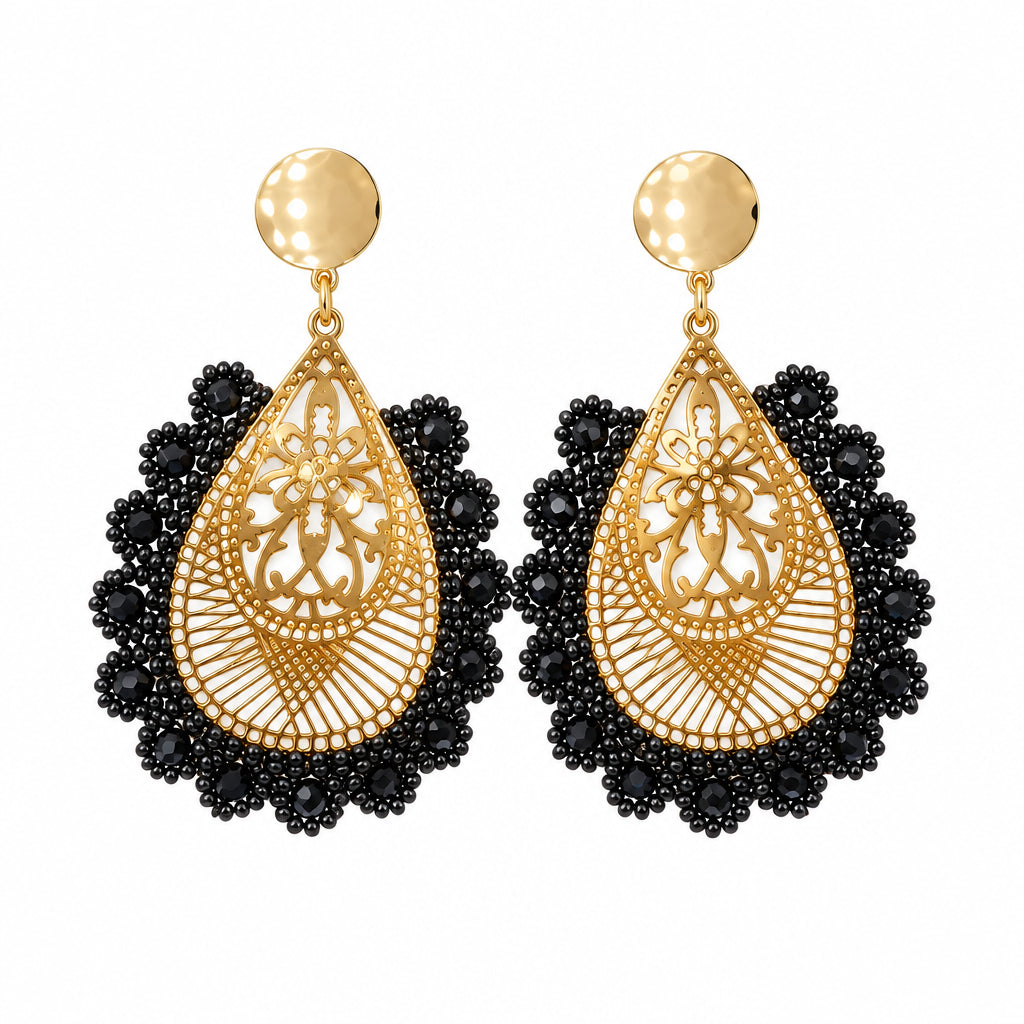 A pair of gold and black teardrop dangle earrings displayed on a small white card against a white bust form.