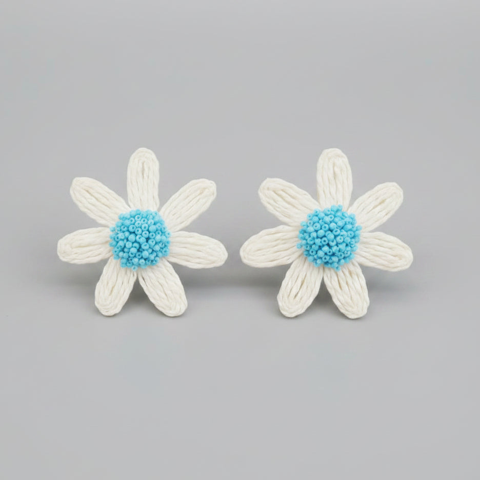 White flower-shaped earrings with blue centers on a metallic surface