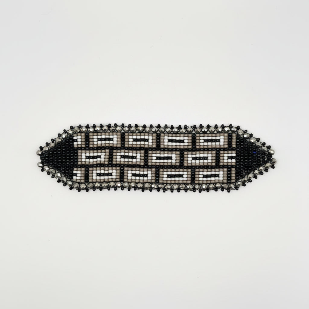 A black and white beaded geometric-patterned bracelet on a brown cardboard hanger tag, photographed against a plain white background.