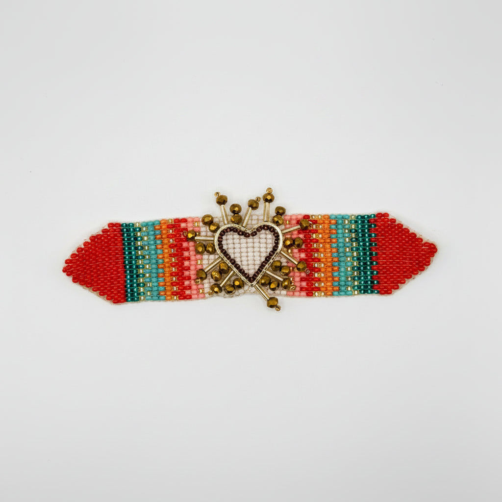 A handmade beaded miyaki bracelet with a central heart-shaped cross-stitch piece and gold-tone crown details, attached to a brown cardboard hanger with a price label of $20.00.