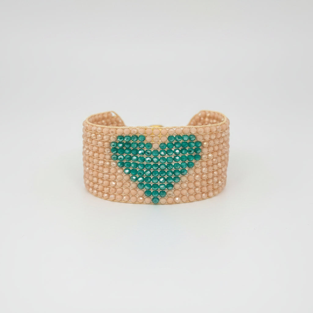 A small woven clutch purse with a peach-beige body, a teal heart design on the front, and a gold-tone clasp, shown with its brown cardboard retail tag on a white background.