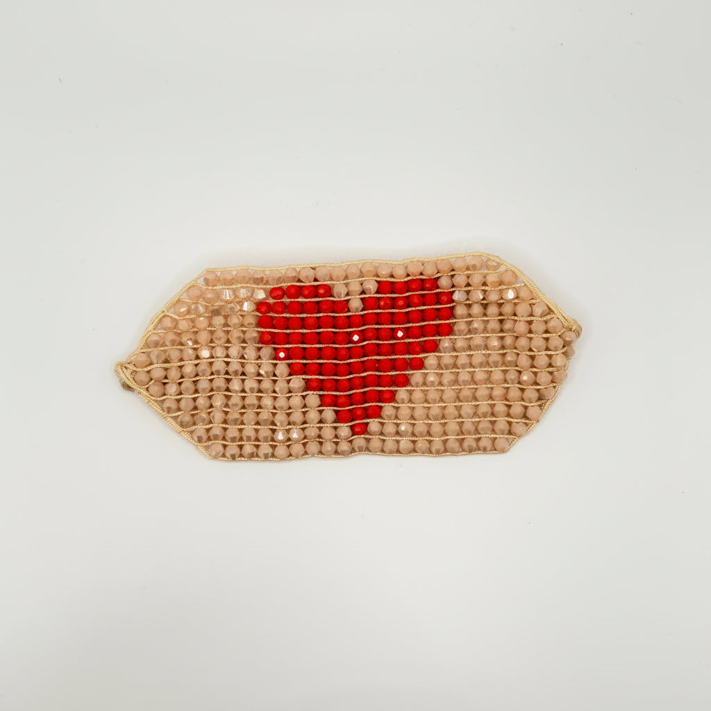A small woven clutch purse with a geometric hexagonal shape, featuring a red heart design on a beige woven background, set against a plain white background.