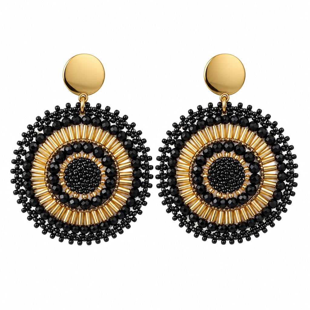 A pair of bohemian-style dangle earrings with intricate black and gold circular patterns, displayed on a small white card against a white background.