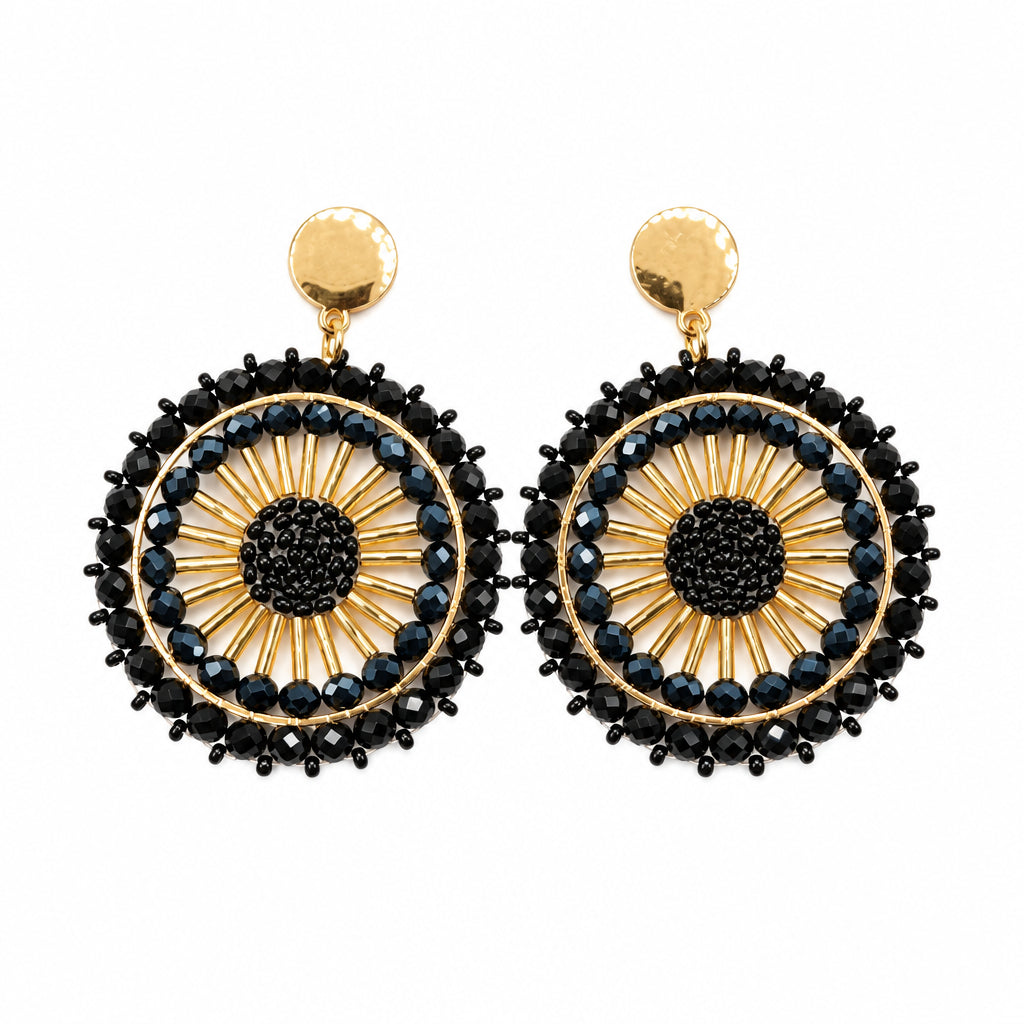 A pair of gold and black beaded dangle earrings with blue accents, displayed on a clear card against a white background.