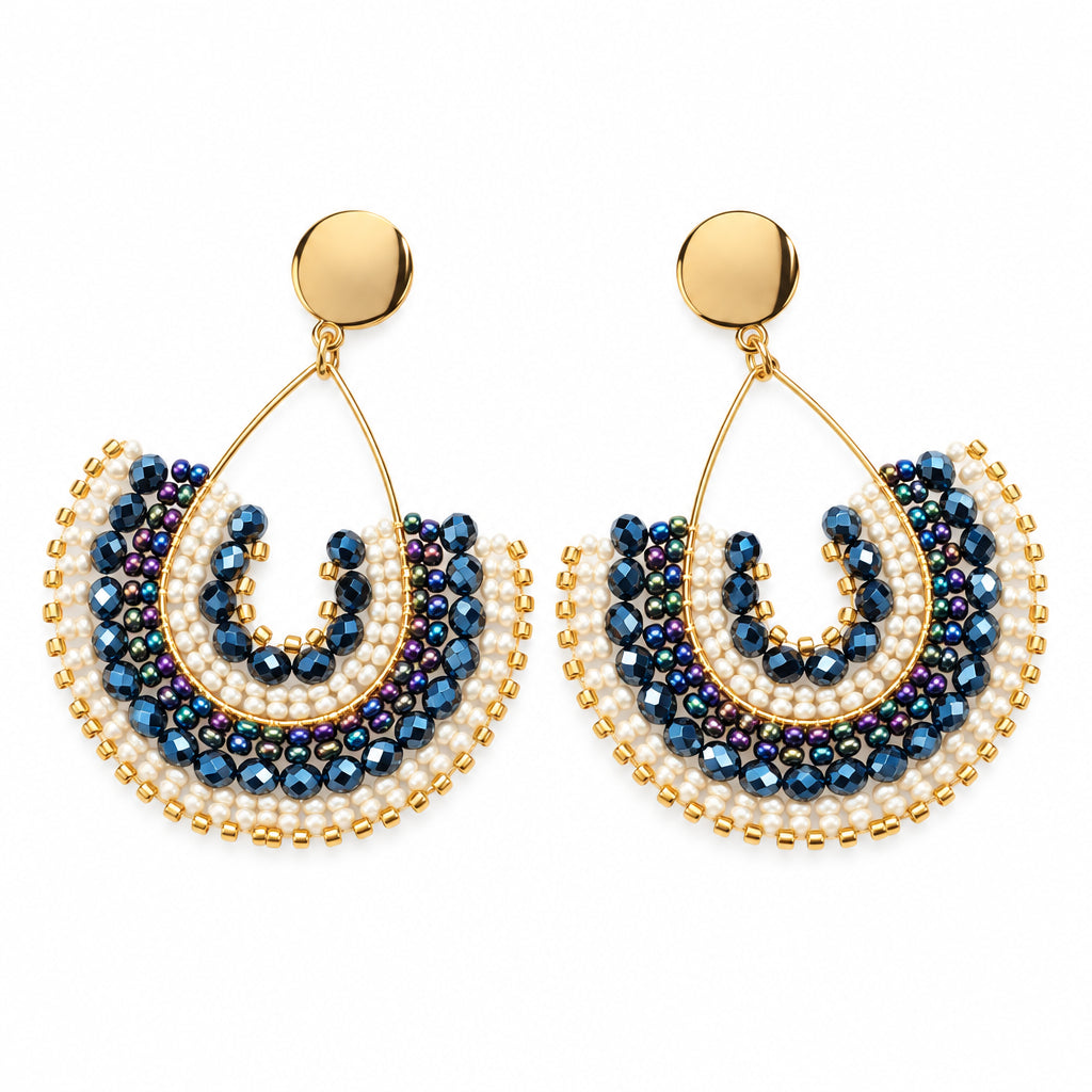A pair of handmade beaded earrings with gold-tone hooks and semi-circular fringe details in navy blue and cream, displayed on a white bust.