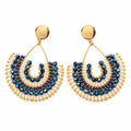 A pair of handmade beaded earrings with gold-tone hooks and semi-circular fringe details in navy blue and cream, displayed on a white bust.