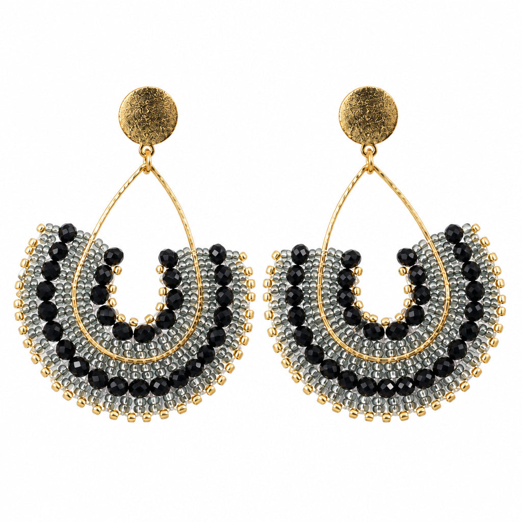 A pair of gold-toned dangle earrings with layered black and silver beaded crescent shapes, displayed on a white jewelry stand.
