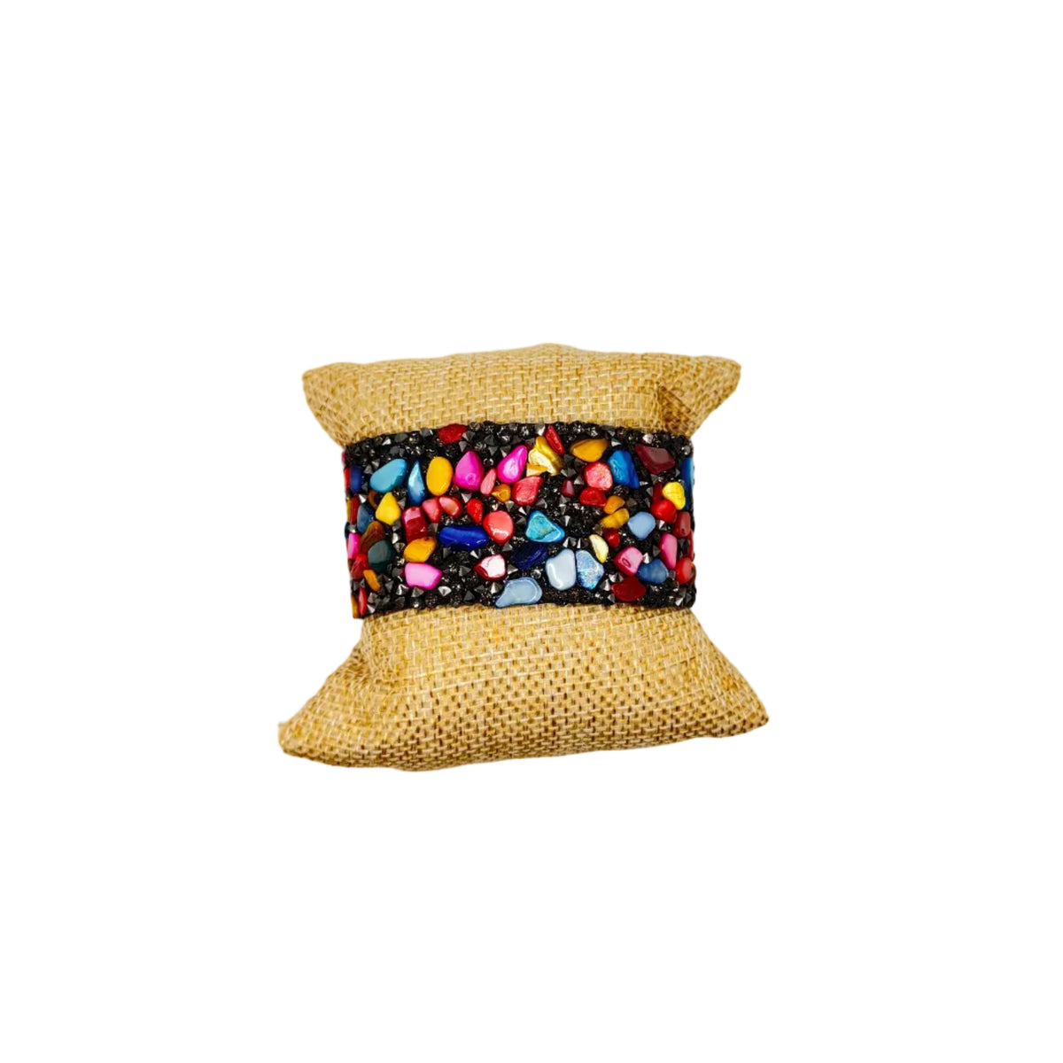 A small decorative fabric pillow or cushion with a natural tan woven fabric body and a colorful patterned band featuring pink, blue, yellow, and white stones on a black background, centered on a plain white background.