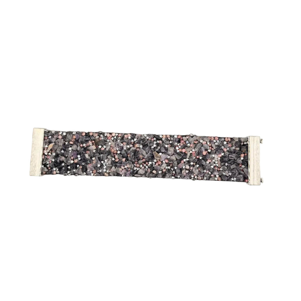 A wide fabric bracelet with a dense multicolor glitter pattern in shades of pink, gold, silver, and black, finished with light beige fabric ends, shown on a plain light gray background.