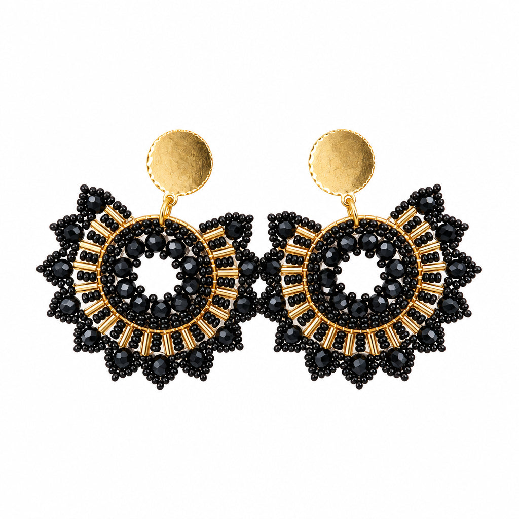 A pair of black and gold beaded dangle earrings displayed on a small white card against a plain light gray background.