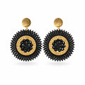 A pair of black and gold statement earrings with textured circular designs, displayed on a white backing card against a white background.
