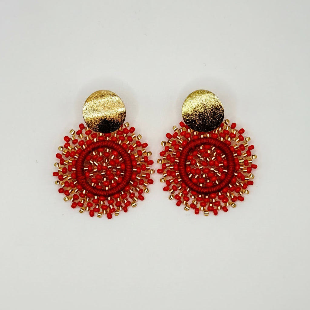 A pair of handmade bohemian-style earrings featuring textured red beaded circular discs with a hammered gold-tone circular stud on top, displayed on a clean white background.
