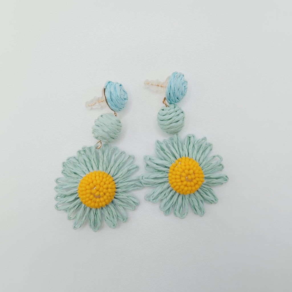 Floral earrings with green leaves and yellow centers on a light gray background